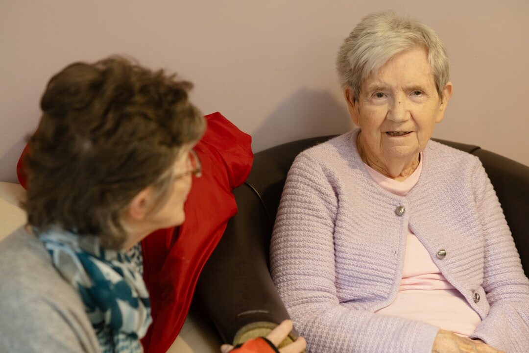 Adult daughter sitting and laughing with her elderly mother at home